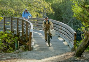 Two men carry fishing gear on their bicycles.