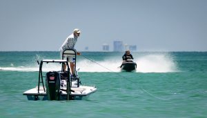 Personal watercraft speeding by a man fishing from a boat.