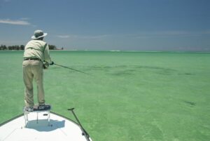 A man stands on the bow of a boat and casts with a fishing rod and reel.